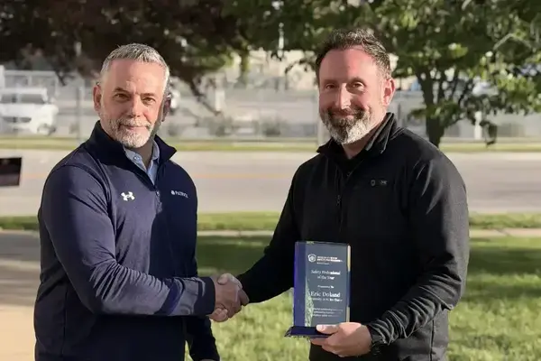 Smiling man in navy quarter-zip shakes hands with Eric Doland, who holds a 'Safety Professional of the Year' award from Notre Dame.