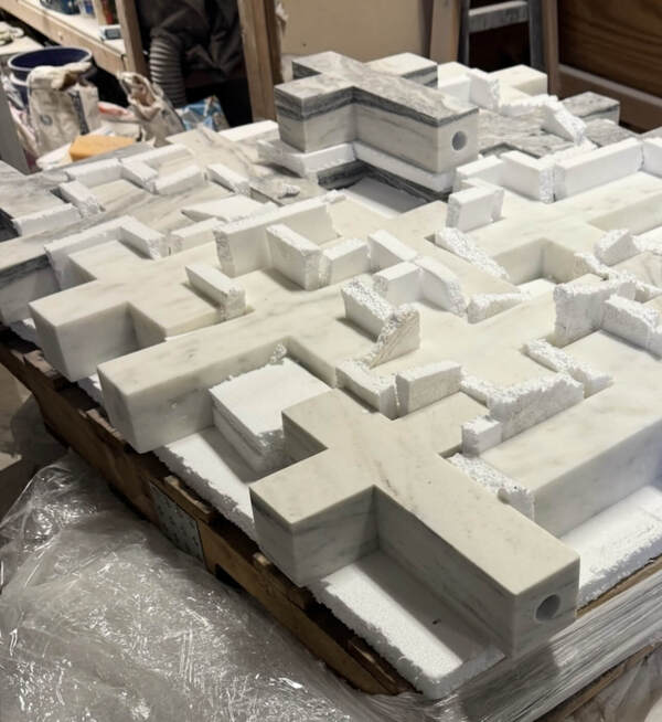 A collection of white and grey marble crosses, some with hollow ends, mixed with white foam pieces on a wood pallet.